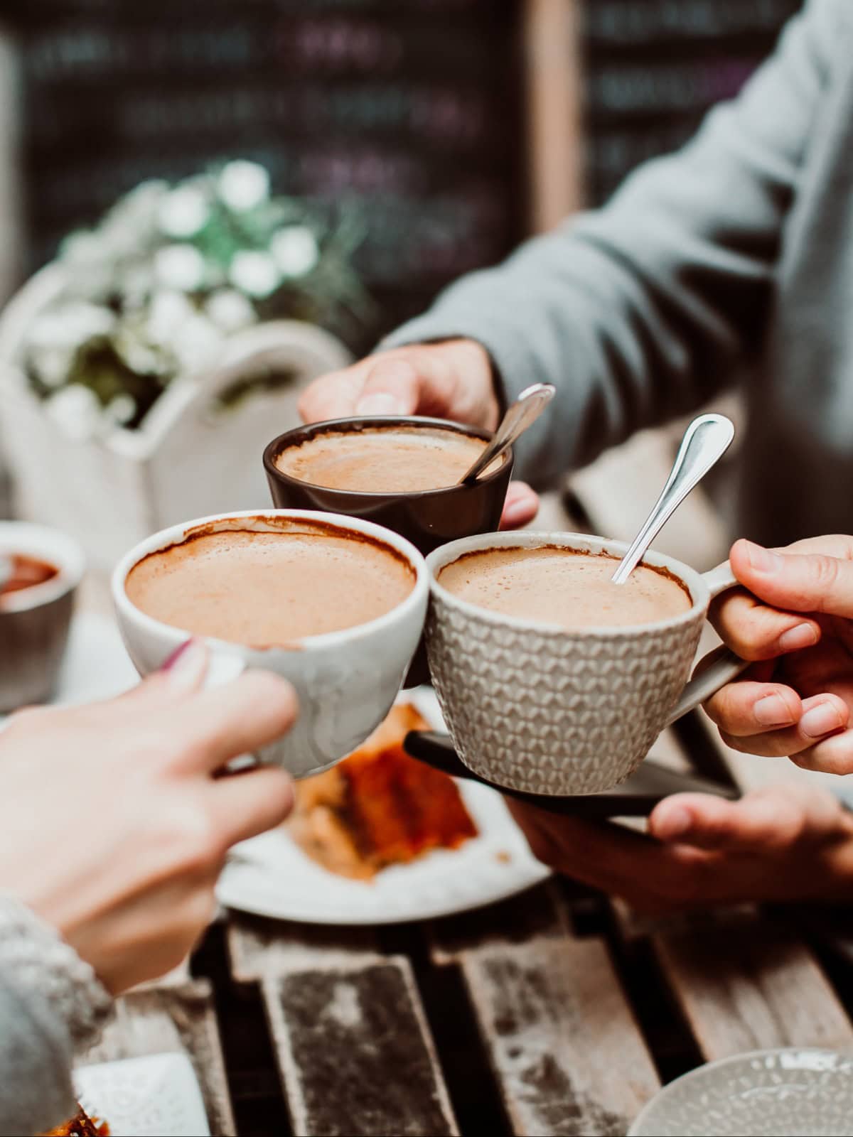 Eine Gruppe junger Freunde trinkt Kaffee mit Kuchen in einem Außenbereich.